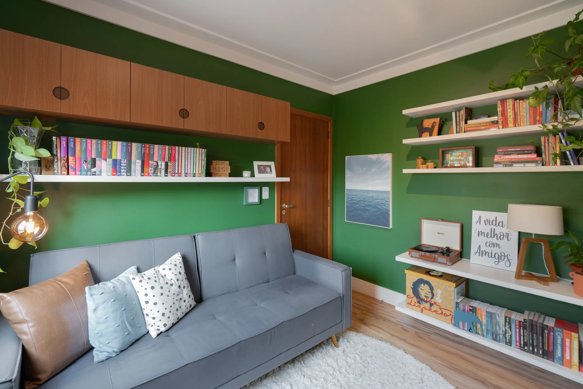 escritório com parede verde, sofá cinza e prateleiras com livros