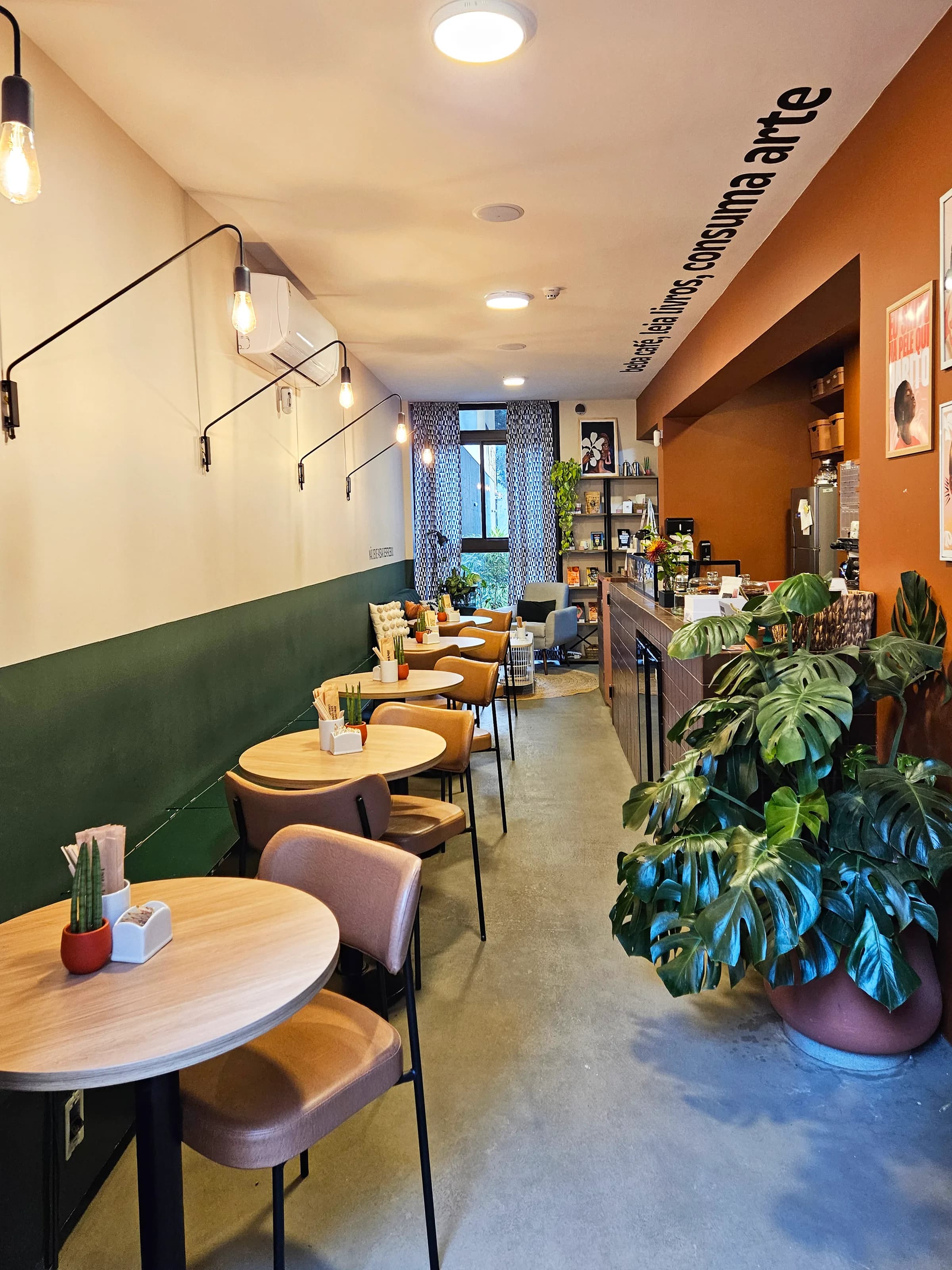 cafeteria estreita com mesas redondas, parede verde e plantas